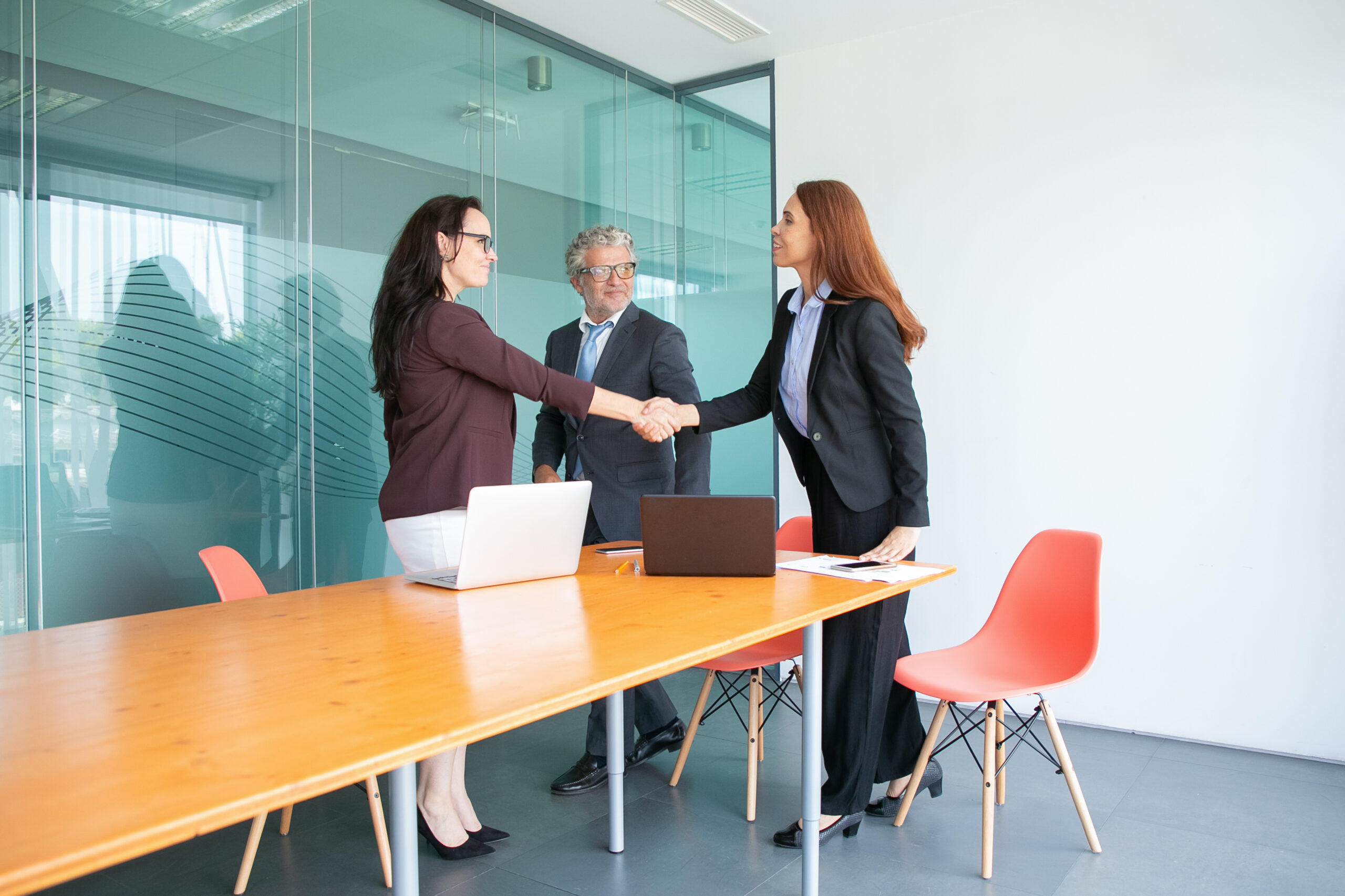 Smiling businesspeople standing and meeting in conference room. Successful content businesswomen handshaking and greeting each other in office. Business and cooperation concept